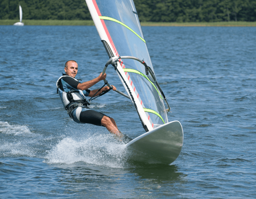 A man windsurfs across a calm body of water.