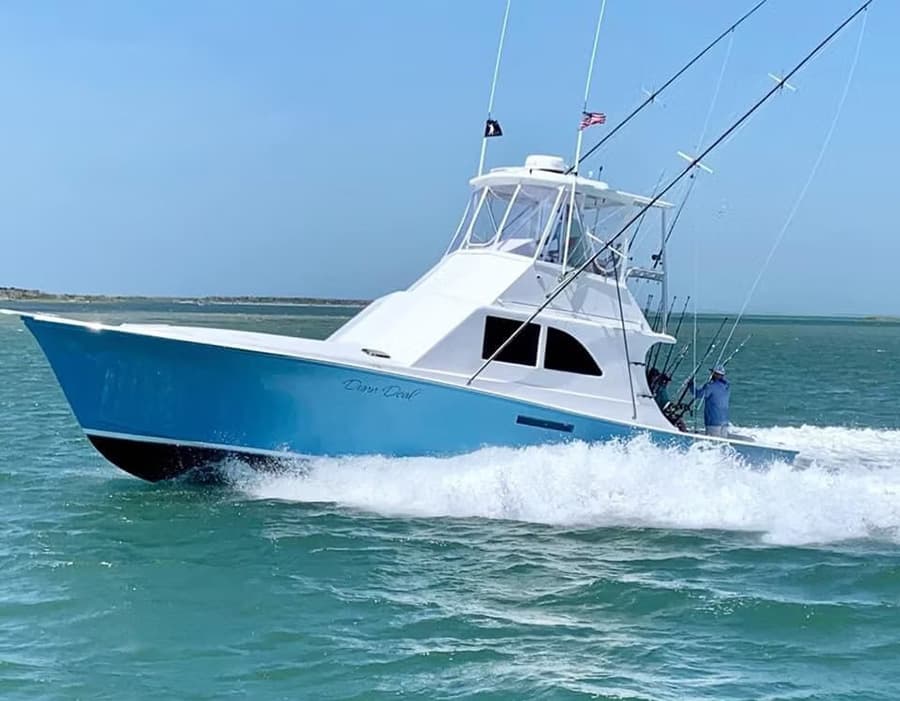 A white and blue motorboat speeds through turquoise water with fishing rods visible.