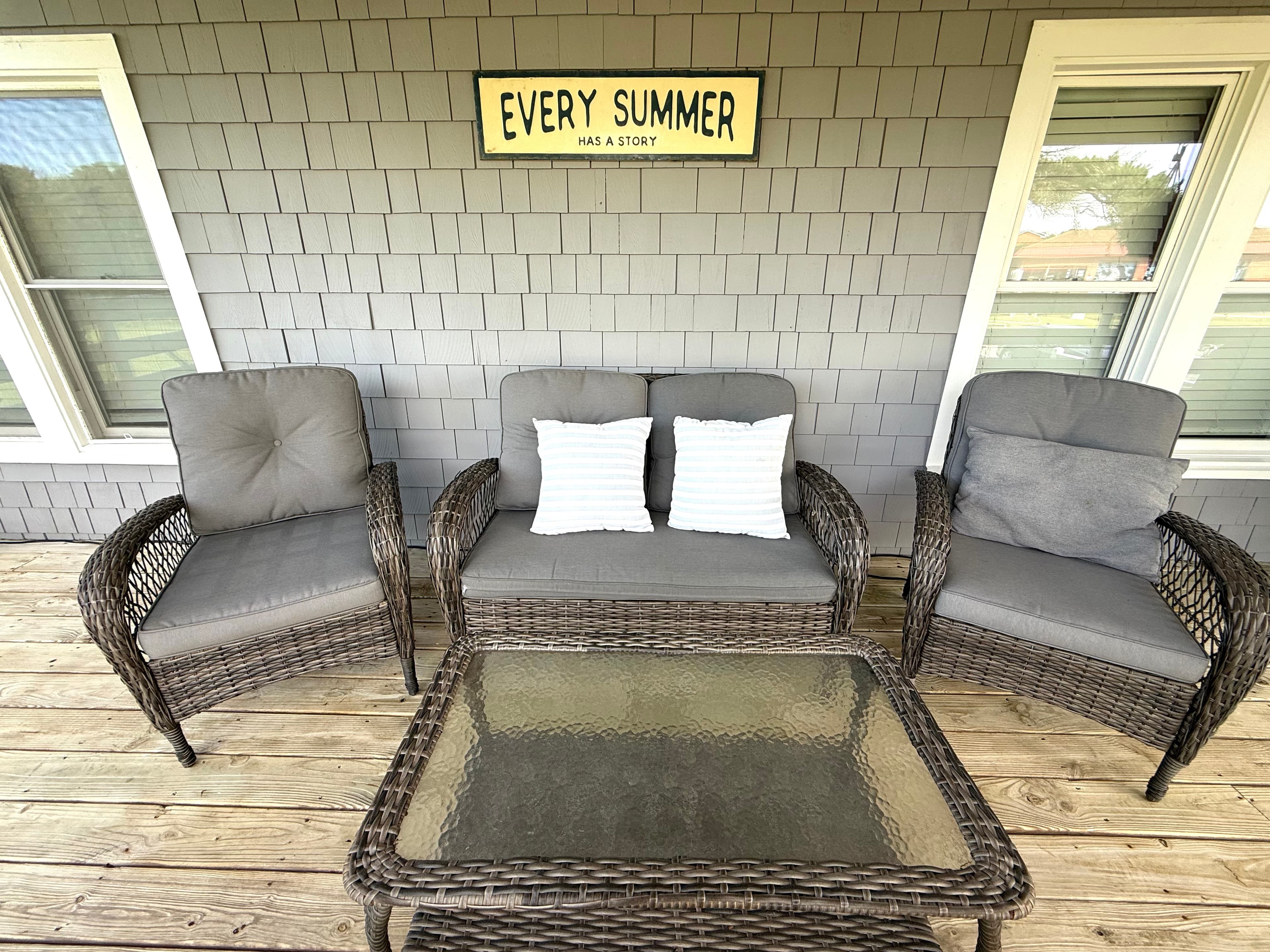 A cozy outdoor seating area with a glass-top table and a sign that reads "EVERY SUMMER HAS A STORY."