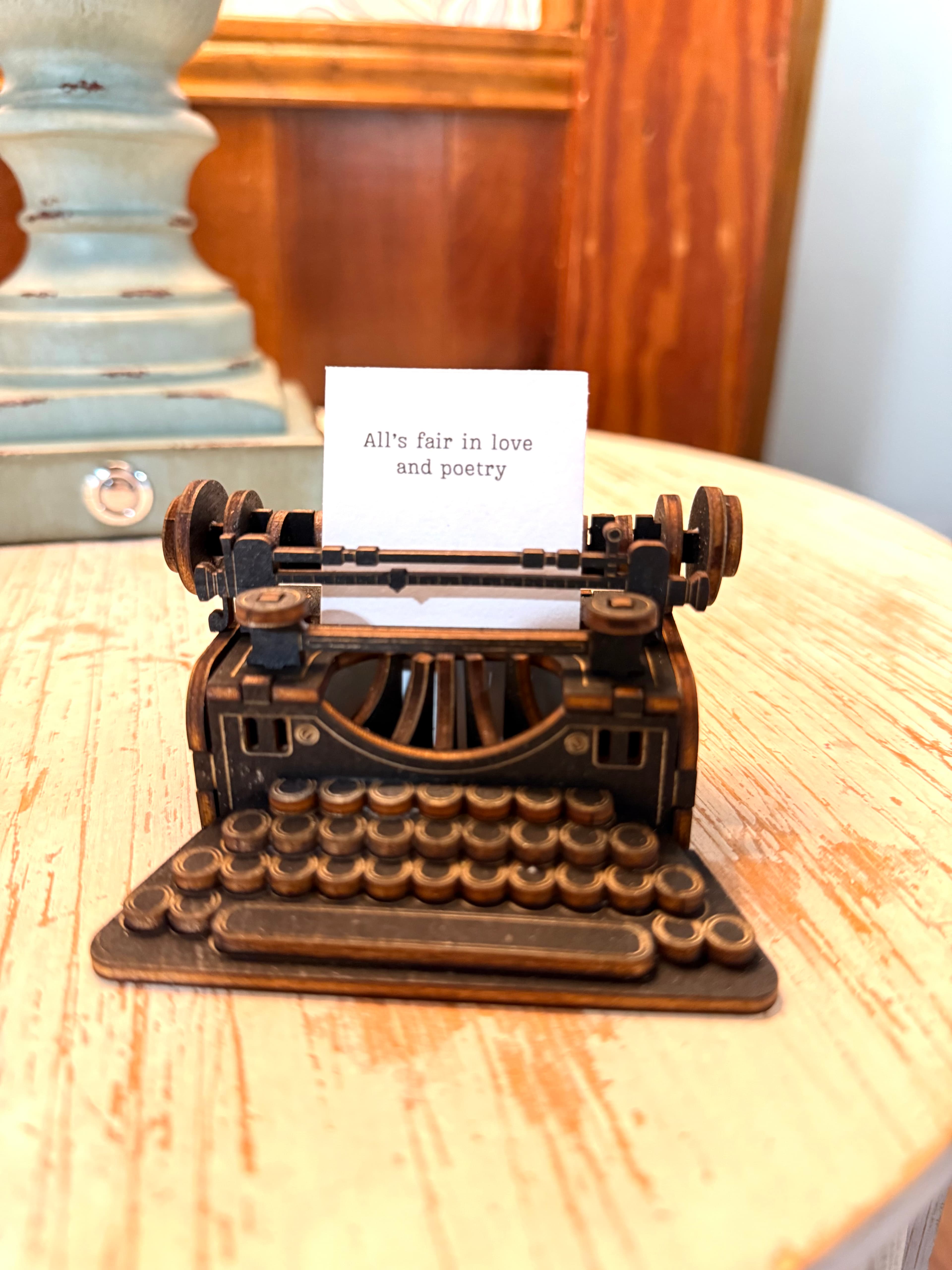 A small vintage-style typewriter displays the phrase "All's fair in love and poetry" on its paper.