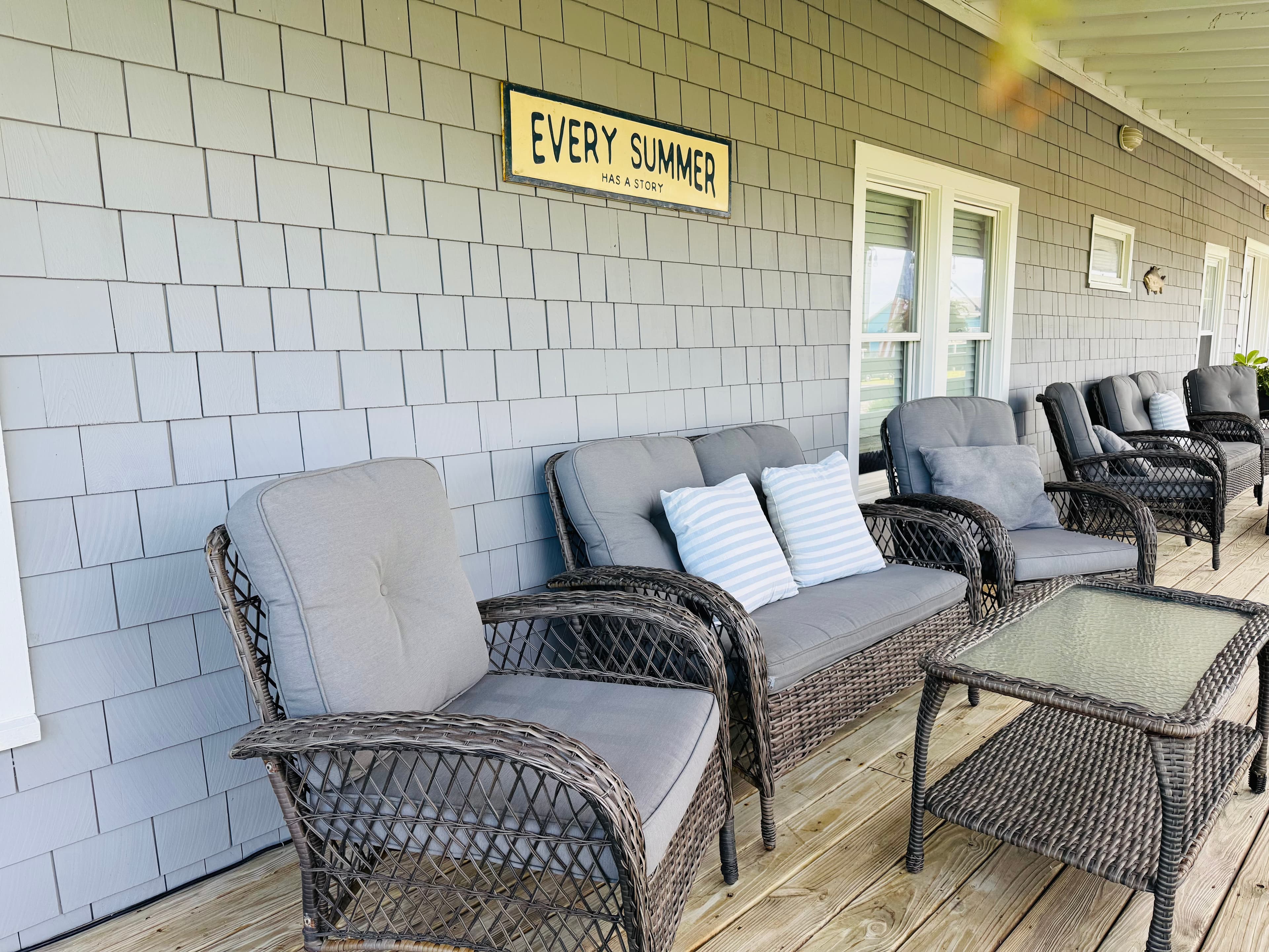A cozy outdoor seating area with wicker furniture and a sign that reads "Every Summer Has a Story."