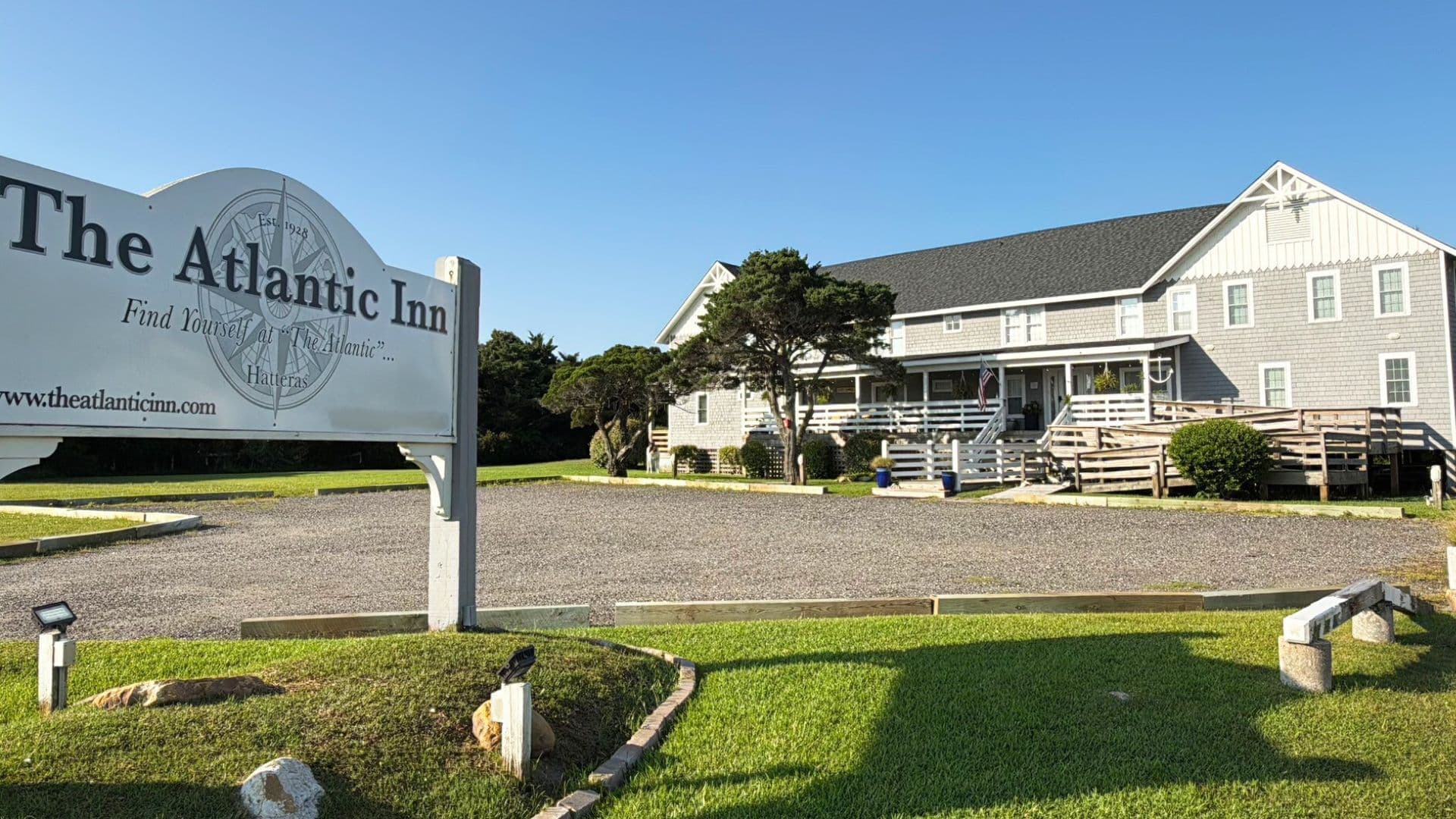 A gray building with a sign reading "The Atlantic Inn" surrounded by green grass and trees.