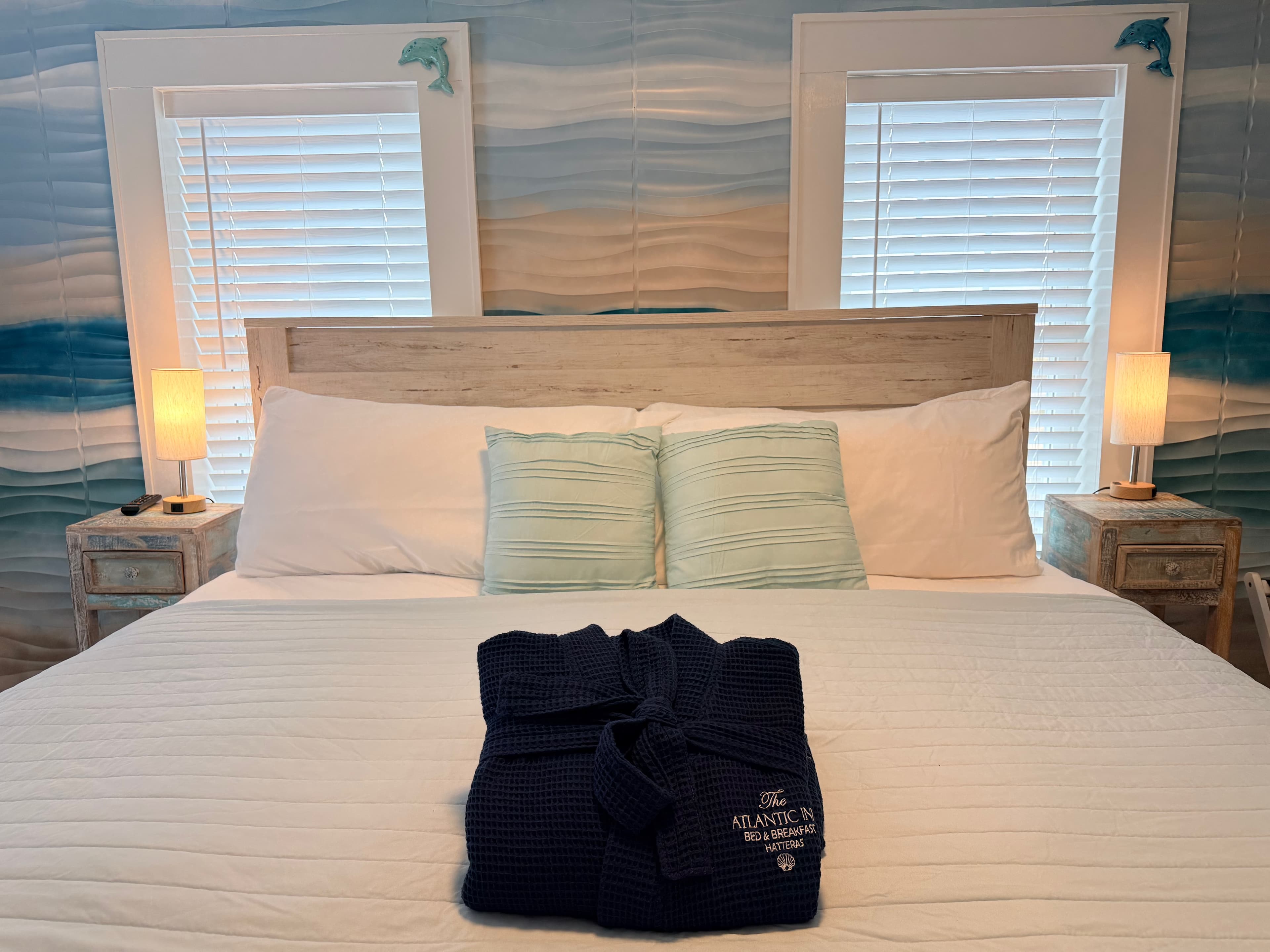 Close up of a bed with light blue bedding and a navy blue bathrobe with the Atlantic Inn logo