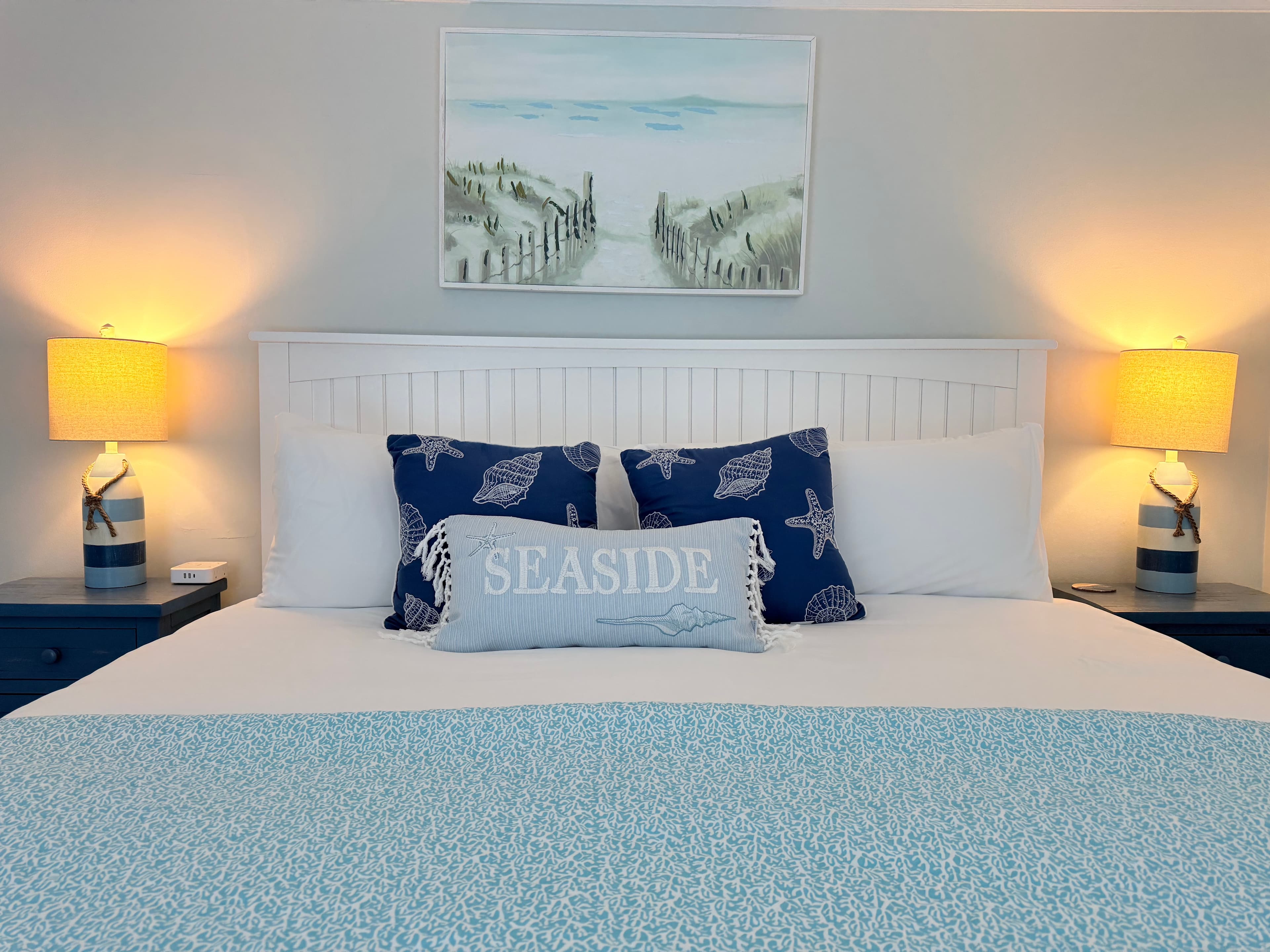 A brightly lit bathroom featuring a white vanity with a louvered cabinet door and a white countertop. The light gray wall is decorated with a black compass decal and a quote, and the room includes a bathtub with a white shower curtain.
