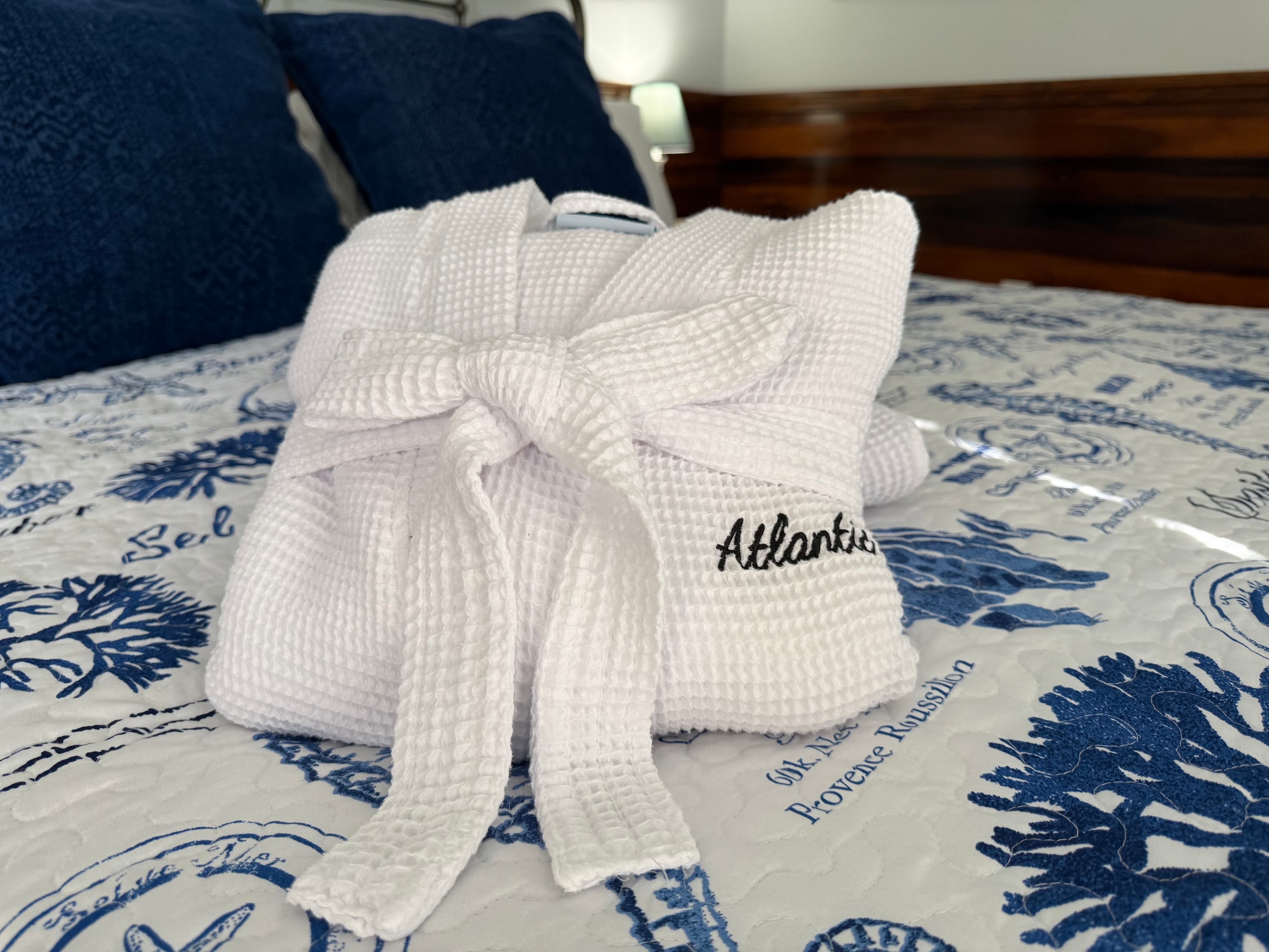 A folded white robe with a tied belt is placed on a blue and white quilted bedspread.