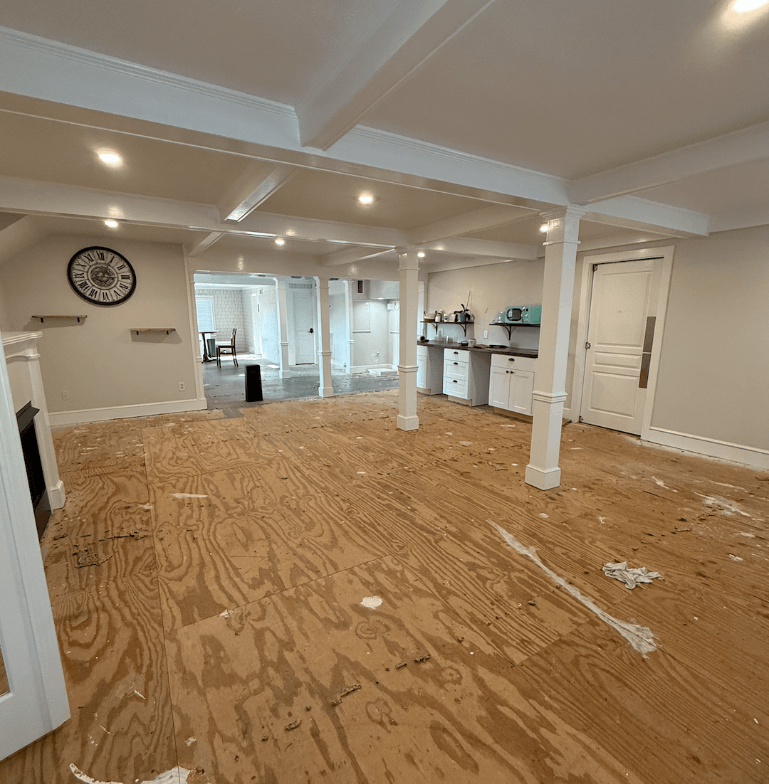 An empty room with wooden floors, white columns, and a kitchen area in the background. An empty room with wooden floors, white columns, and a kitchen area in the background.