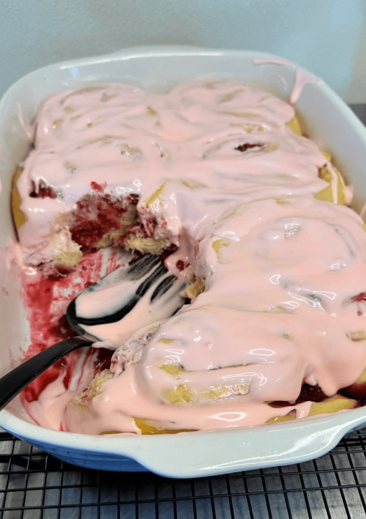 A dish of pink frosted cake with portions removed and a spoon resting inside.