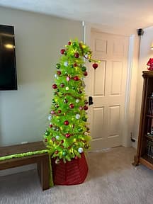 A colorful, green Christmas tree with red and silver ornaments stands in a corner by a closed door.
