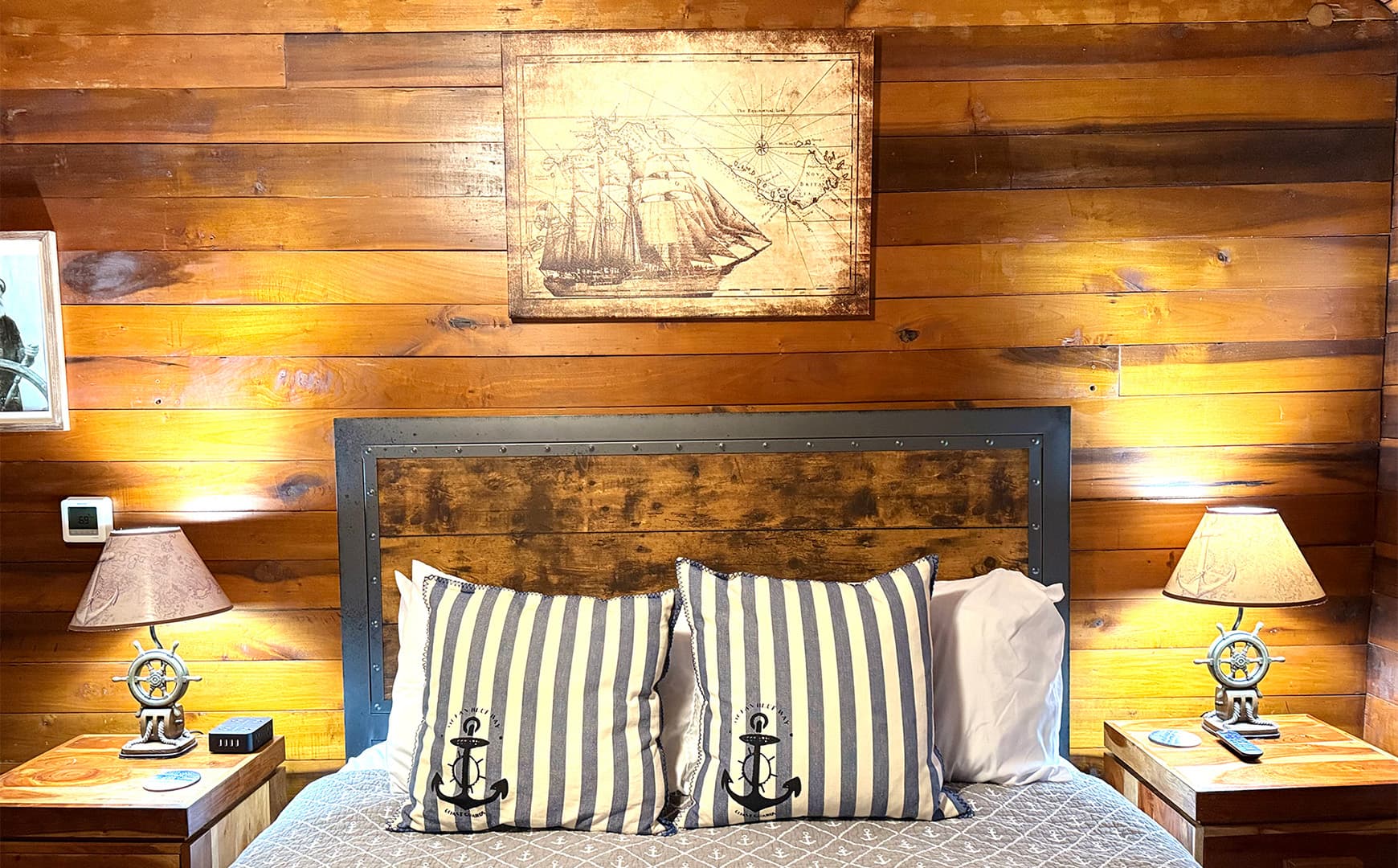 A cozy bedroom featuring a wooden wall, a nautical-themed bed with striped pillows, and bedside lamps.