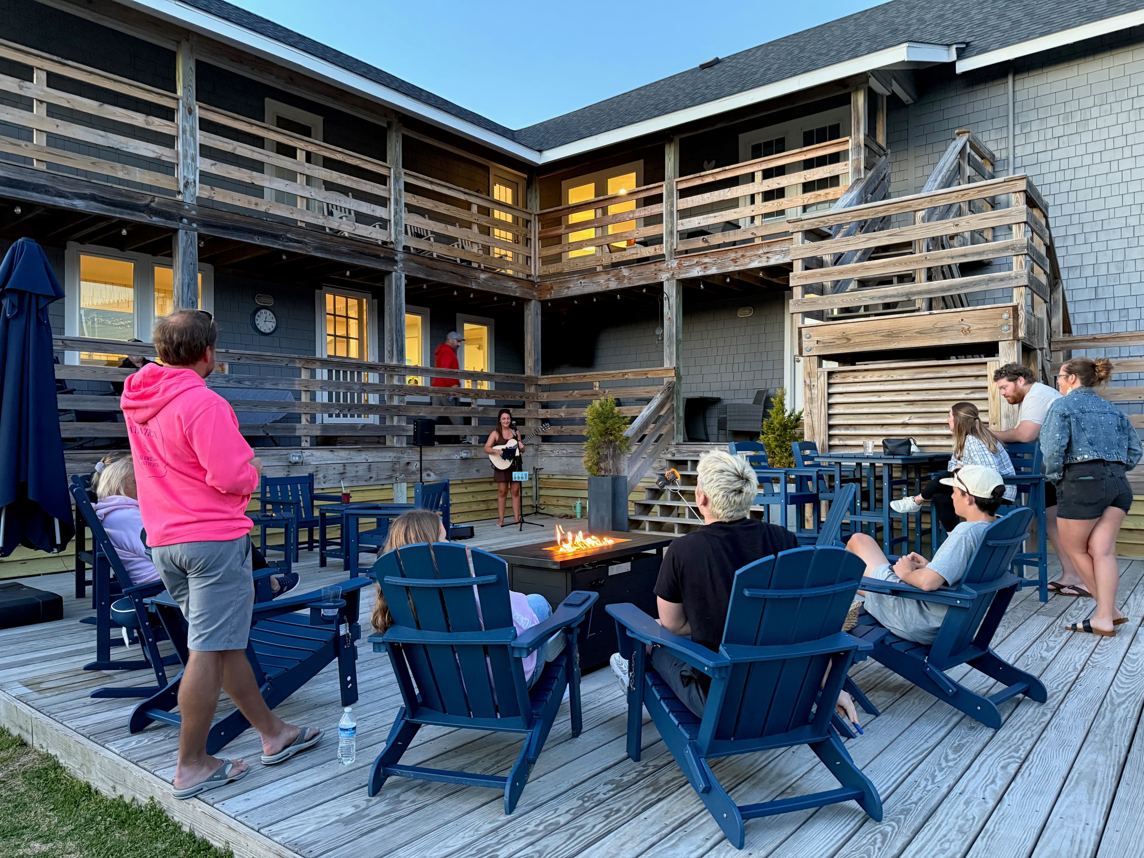 A group of people gathers around a fire pit on a deck, enjoying an evening together.