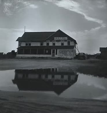 A weathered building and its reflection in a puddle under a cloudy sky.