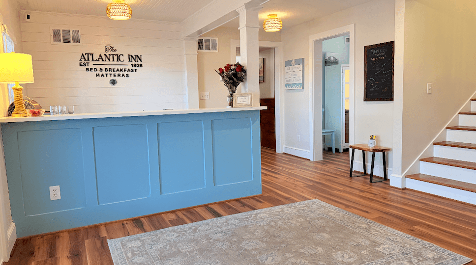 Interior view of The Atlantic Inn's reception area with blue check-in counter, wooden flooring, and light fixtures. Interior view of The Atlantic Inn's reception area with blue check-in counter, wooden flooring, and light fixtures.