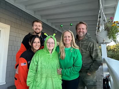 A group of five people dressed in colorful costumes poses together on a porch.