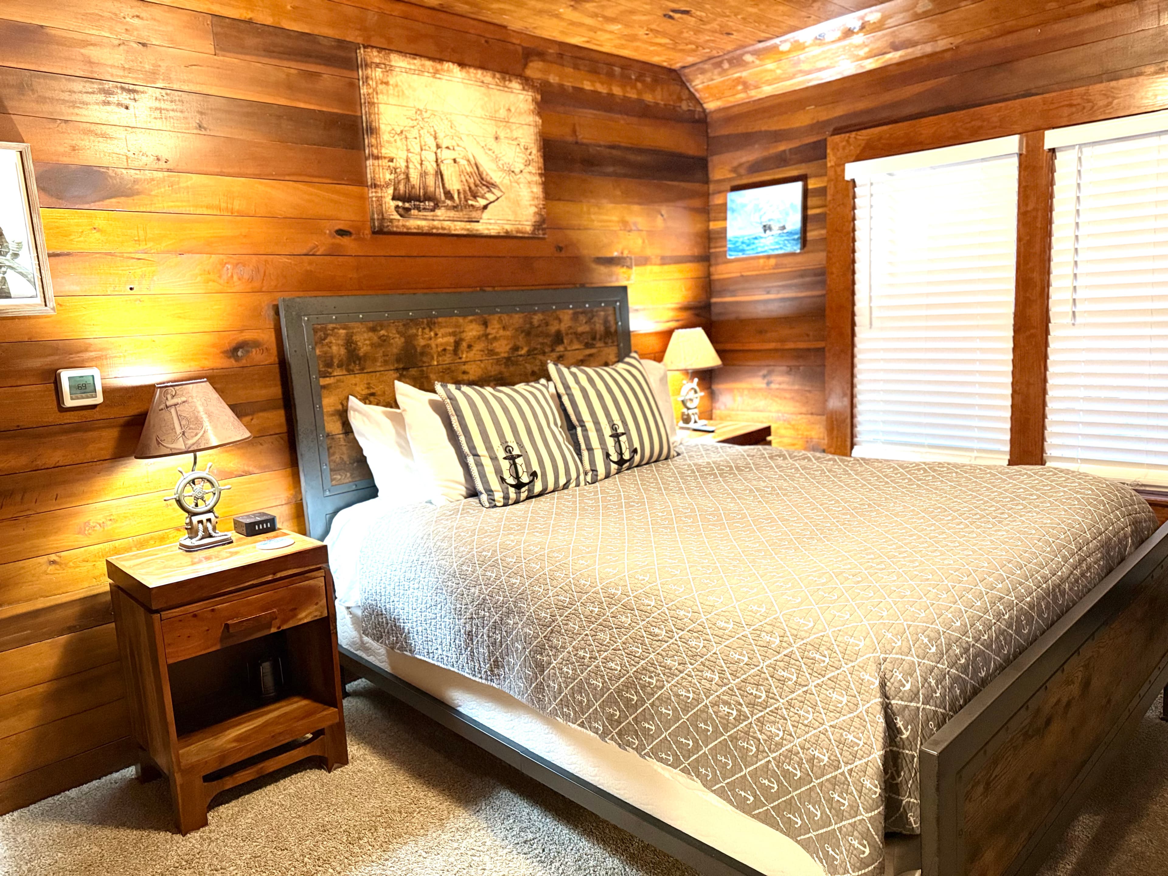 Cozy wooden bedroom featuring a queen-sized bed with nautical-themed pillows and soft lighting.