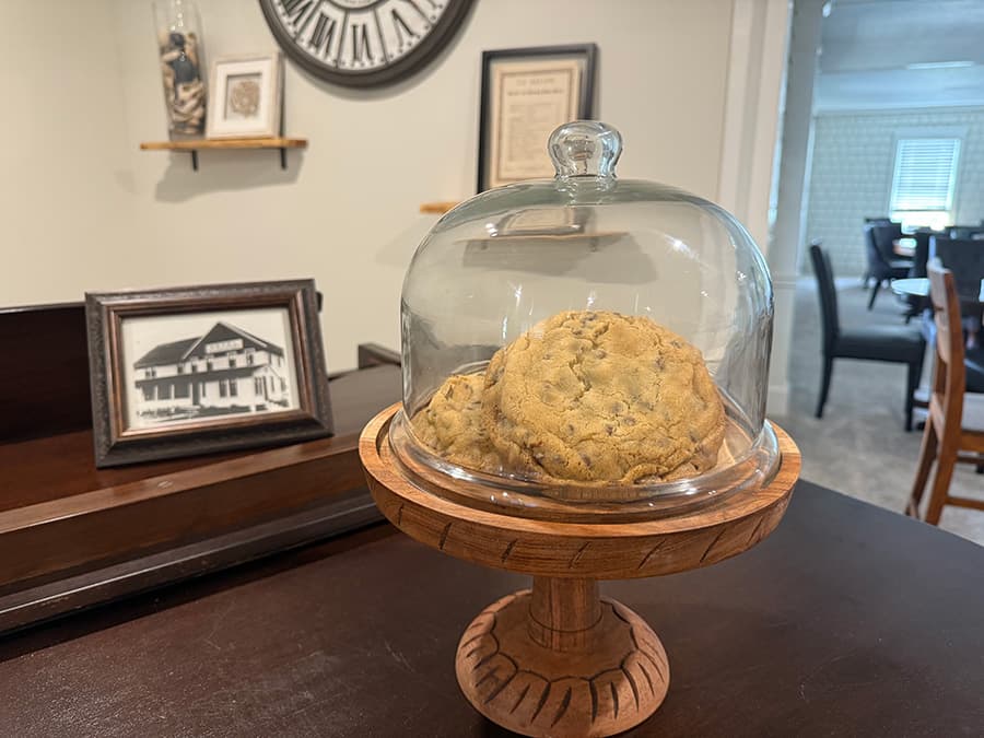 A cookie placed under a glass cloche on a wooden pedestal in a cozy, well-decorated room.