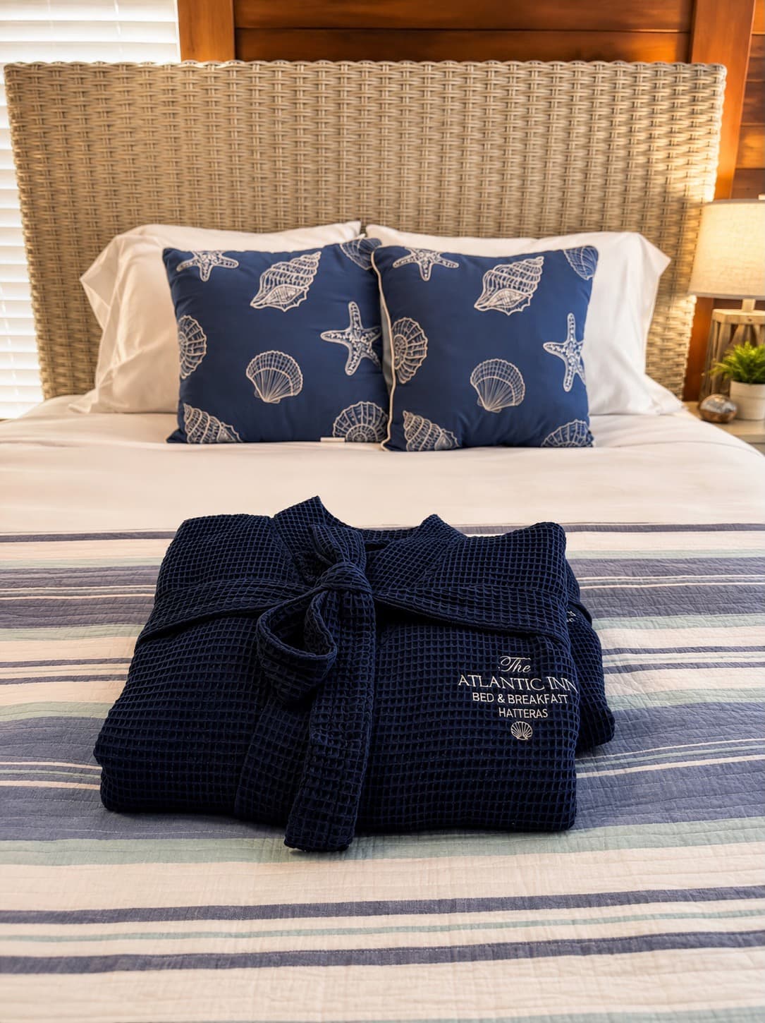 A neatly folded navy bathrobe is displayed on a striped bedspread, with patterned pillows in the background.