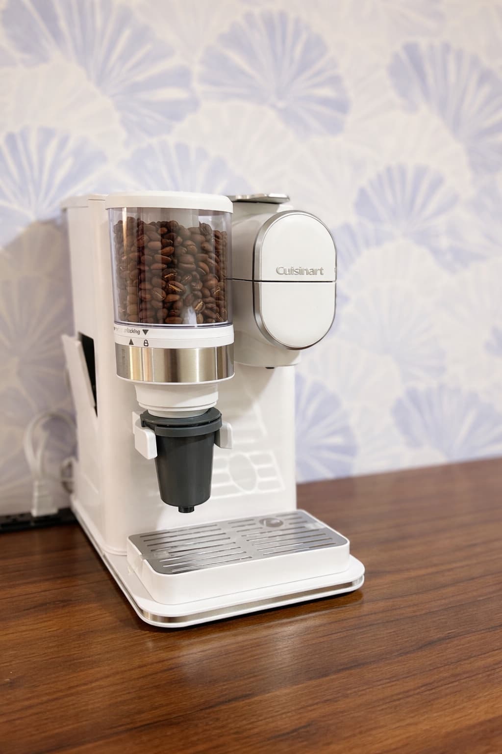 A white Cuisinart coffee grinder and brewer sits on a wooden countertop against a light patterned wall.