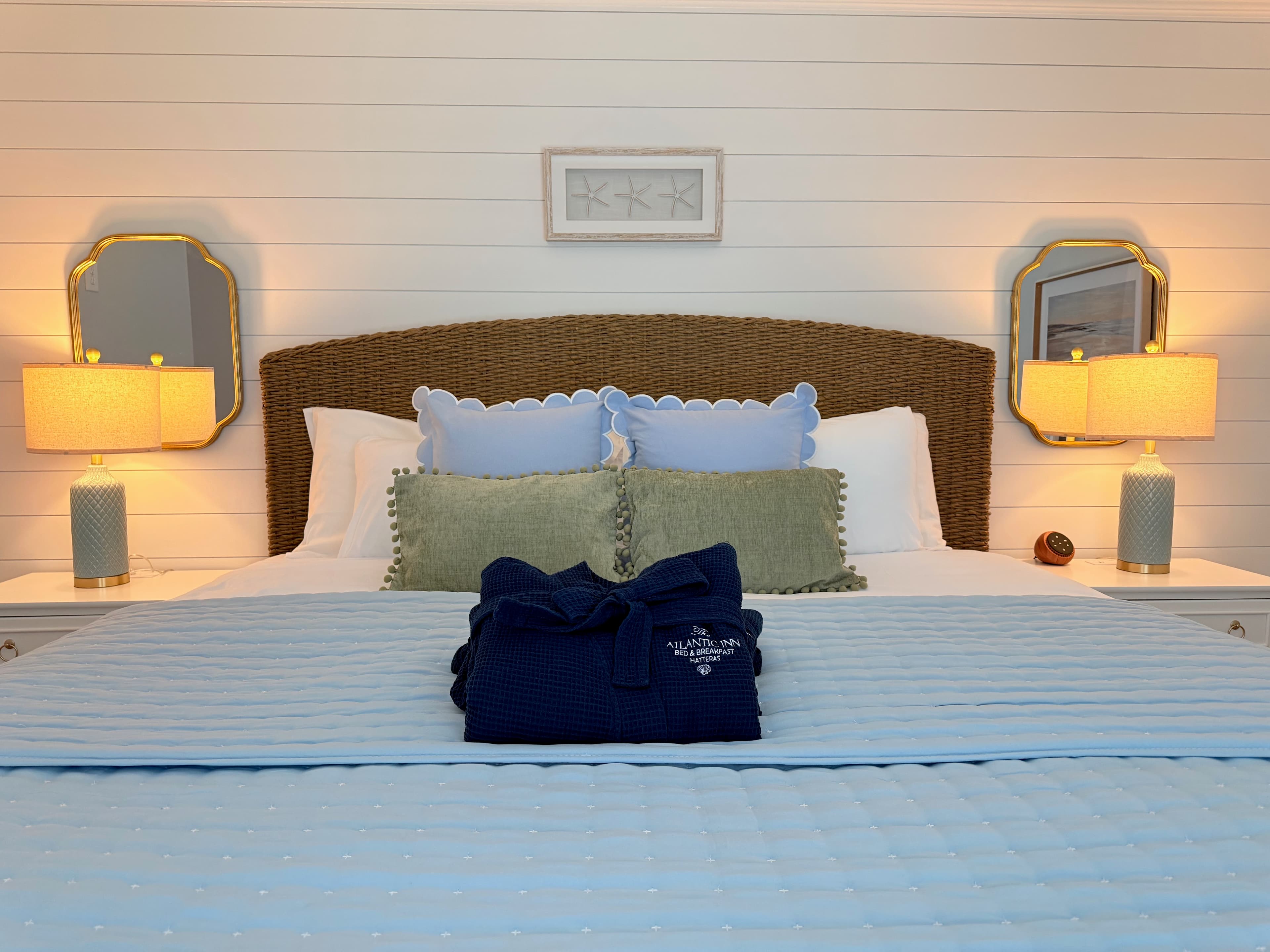 A neatly made bed with decorative pillows, two lamps, and a folded robe on a blue quilt.
