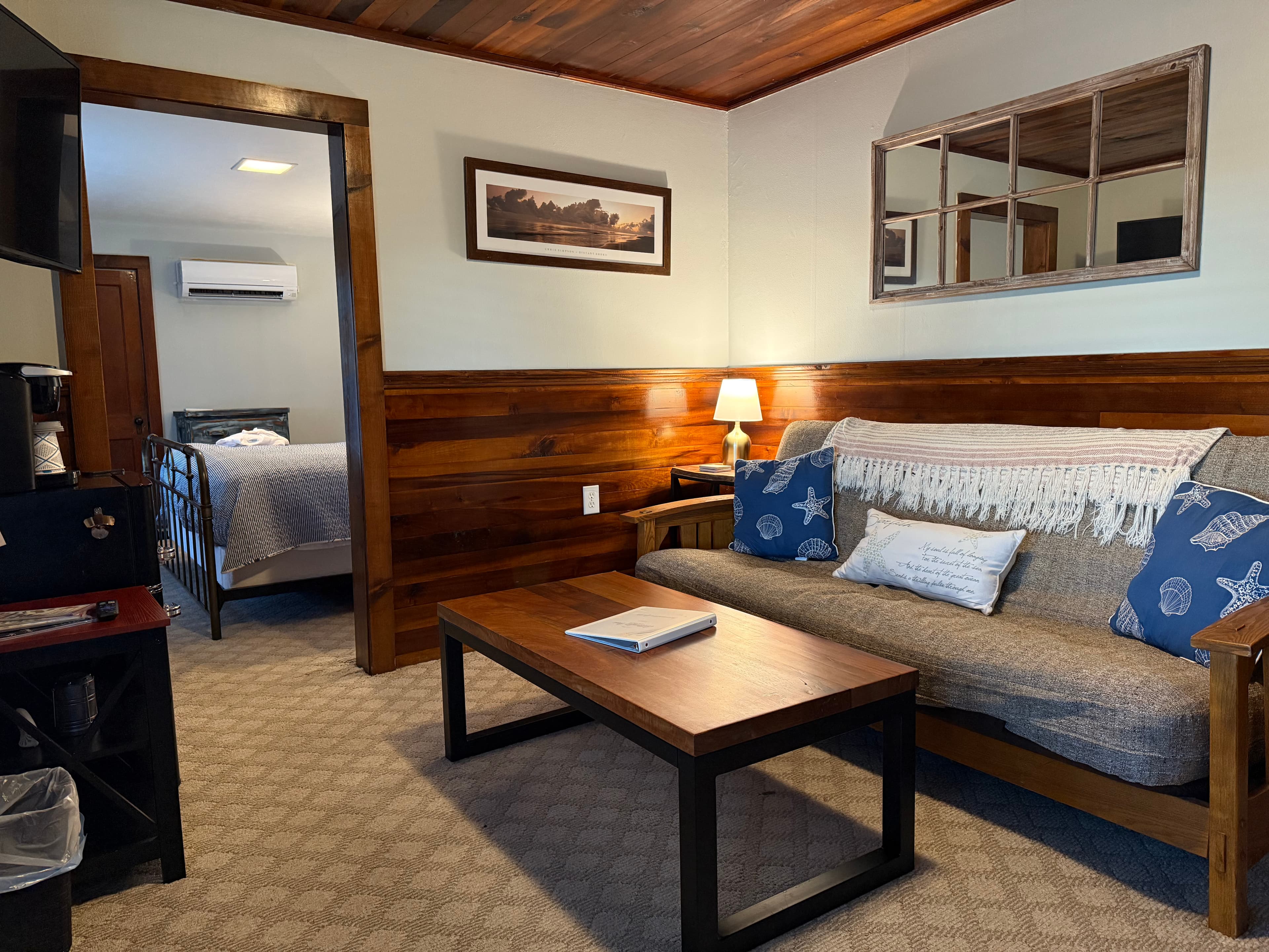 Cozy living area featuring a sofa, coffee table, lamp, and a view into a bedroom.