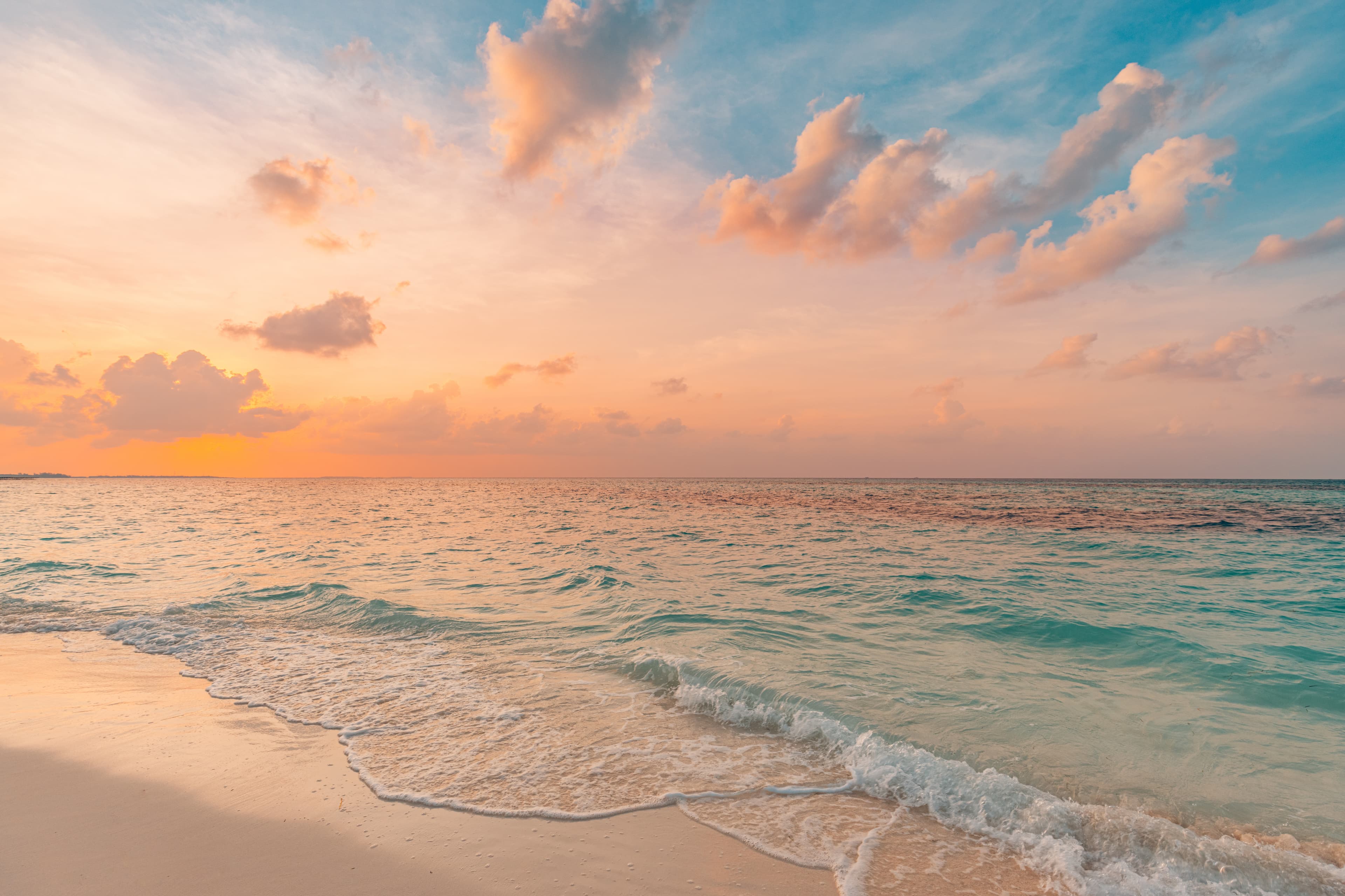 A tranquil beach at sunset with gentle waves lapping at the shore under a colorful sky.