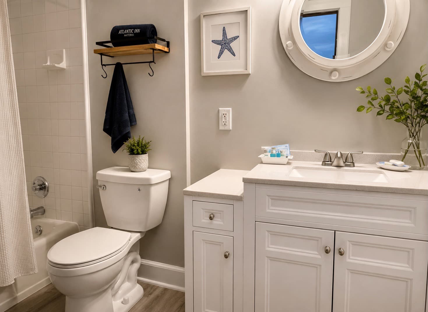 A modern bathroom featuring a white vanity, a round mirror, a toilet, and coastal-themed decor.