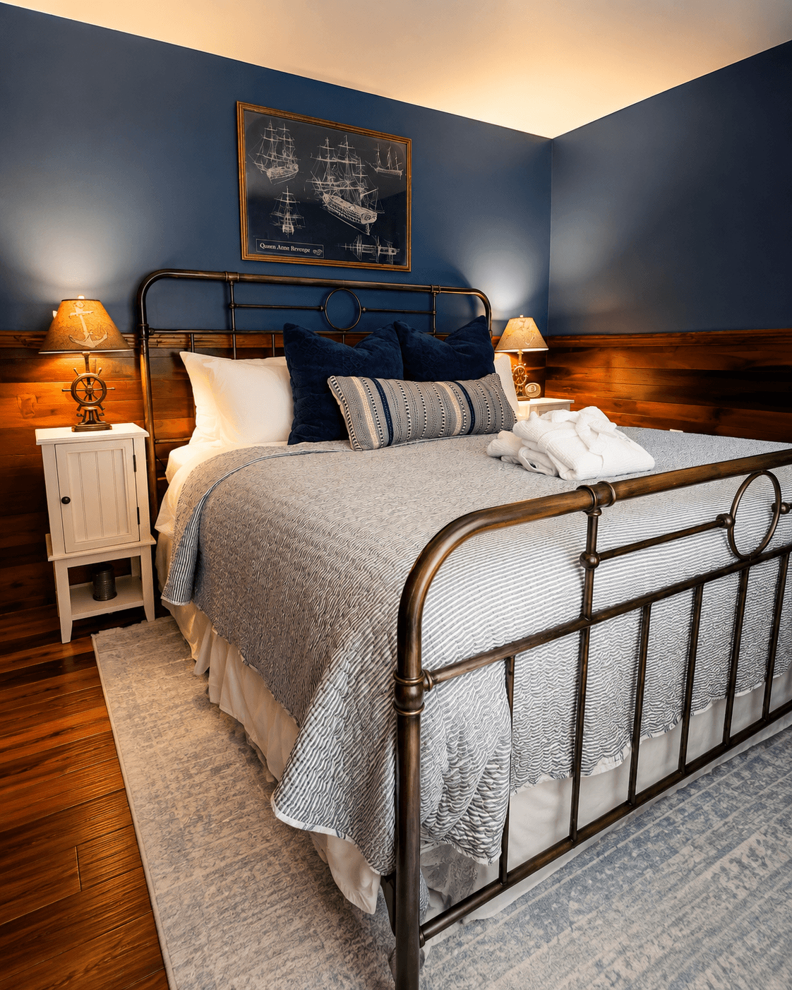 A rustic bedroom at The Atlantic Inn featuring a large bed with nautical seashell-patterned bedding and an iron headboard, set against walls with original dark wood paneling and coastal artwork.