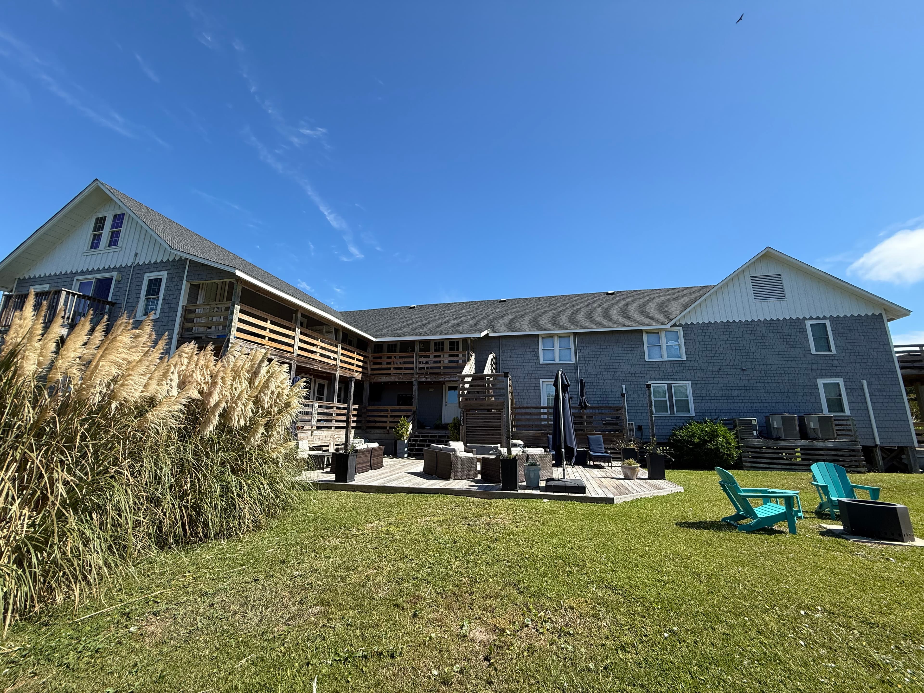 A gray building with outdoor seating areas and grass in the foreground under a clear blue sky.