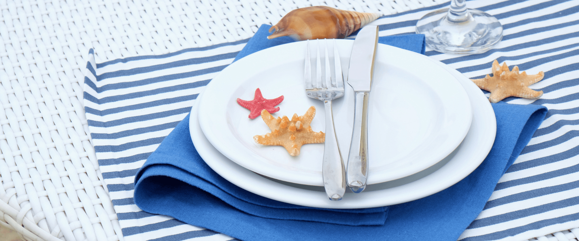 A neatly arranged table setting with plates, cutlery, and decorative starfish on a blue napkin.