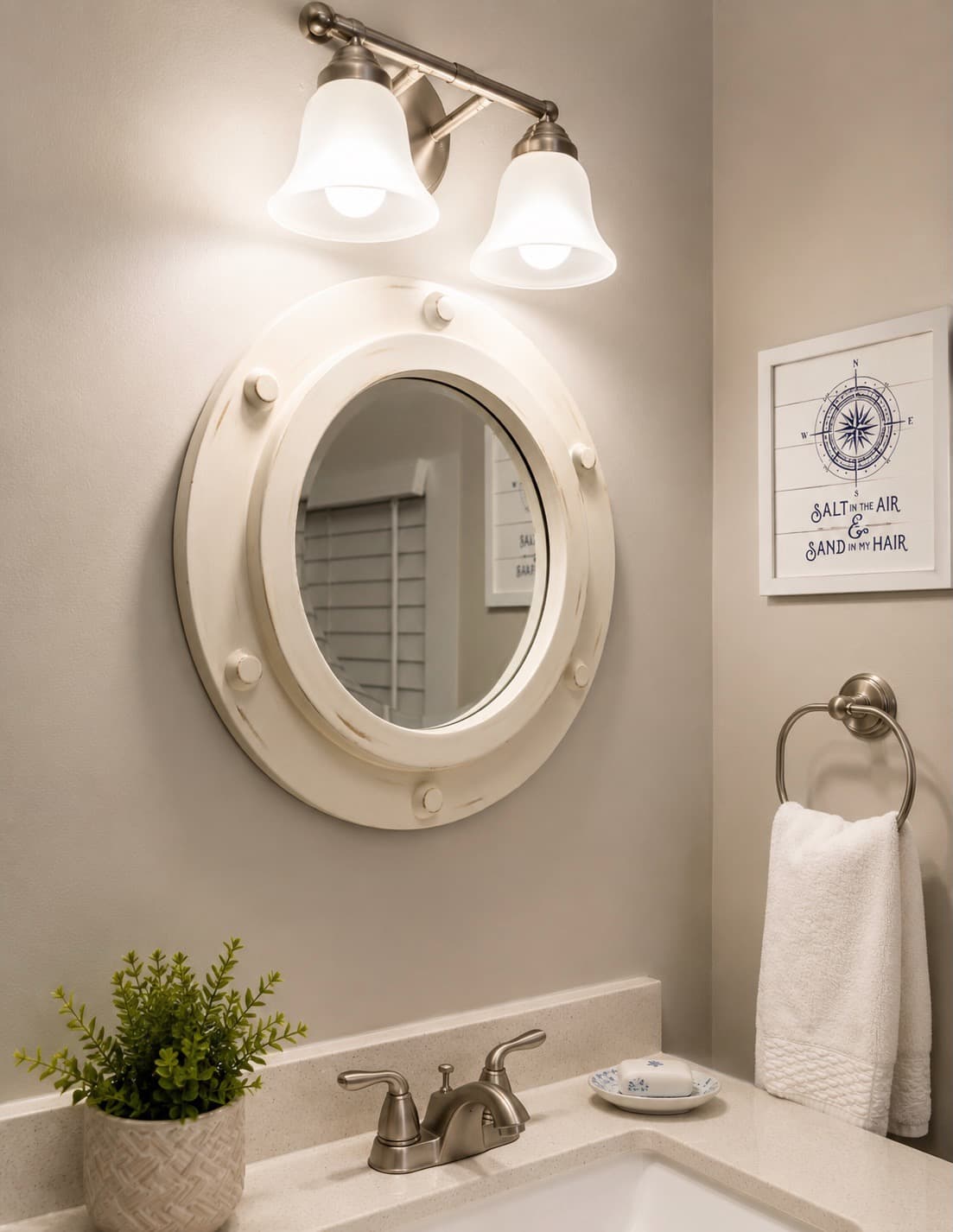 A stylish bathroom featuring a round mirror, light fixtures, a small plant, and decorative wall art.