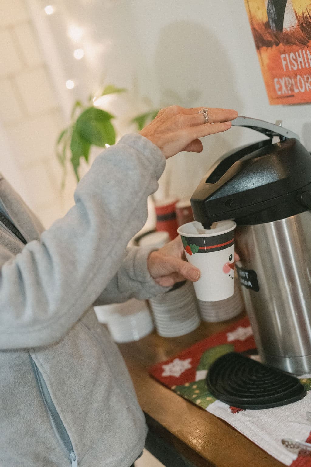 A person pours a drink from a coffee server into a festive cup on a wooden table.