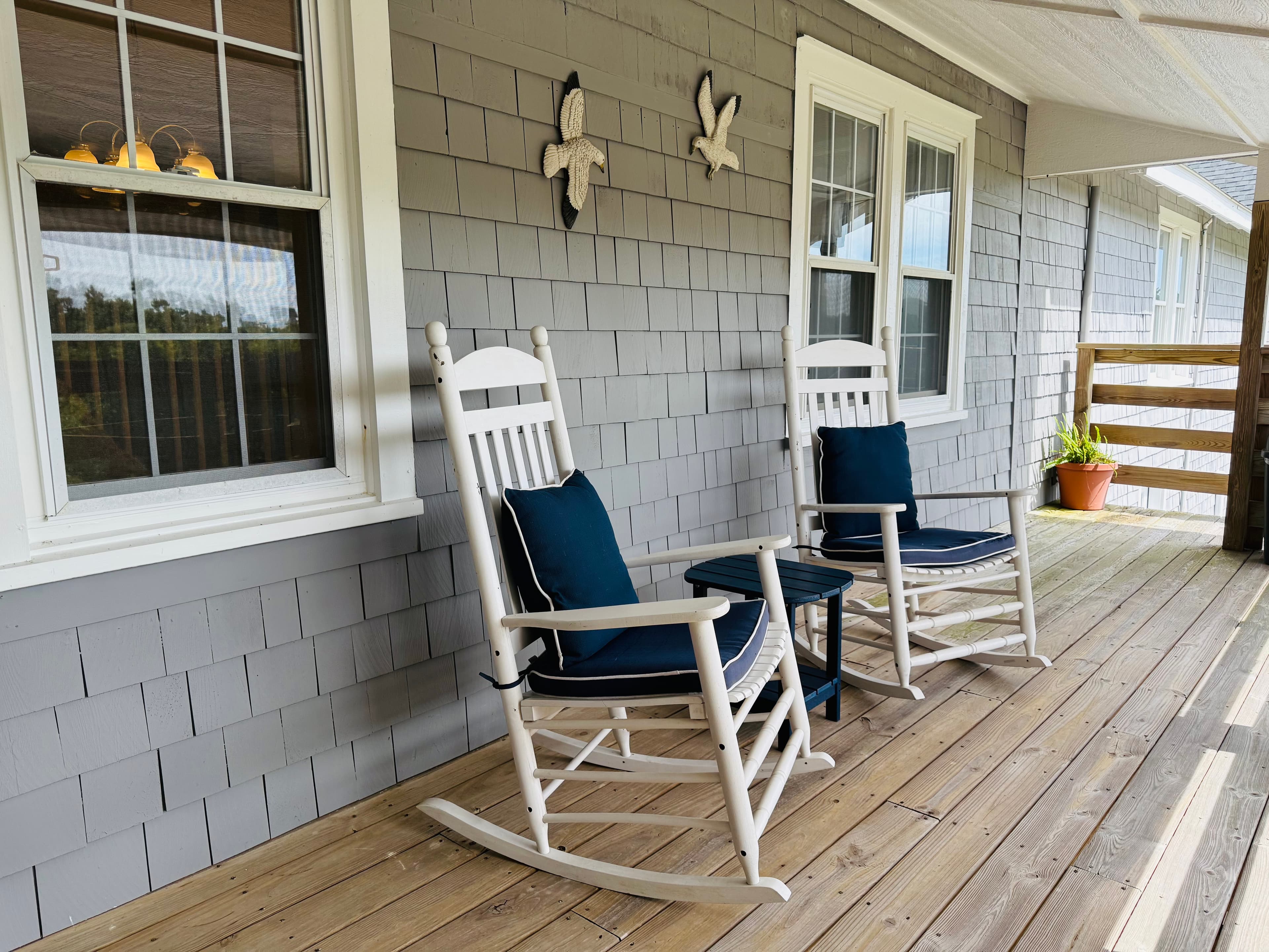 Two white rocking chairs with blue cushions and a small table on a wooden porch.