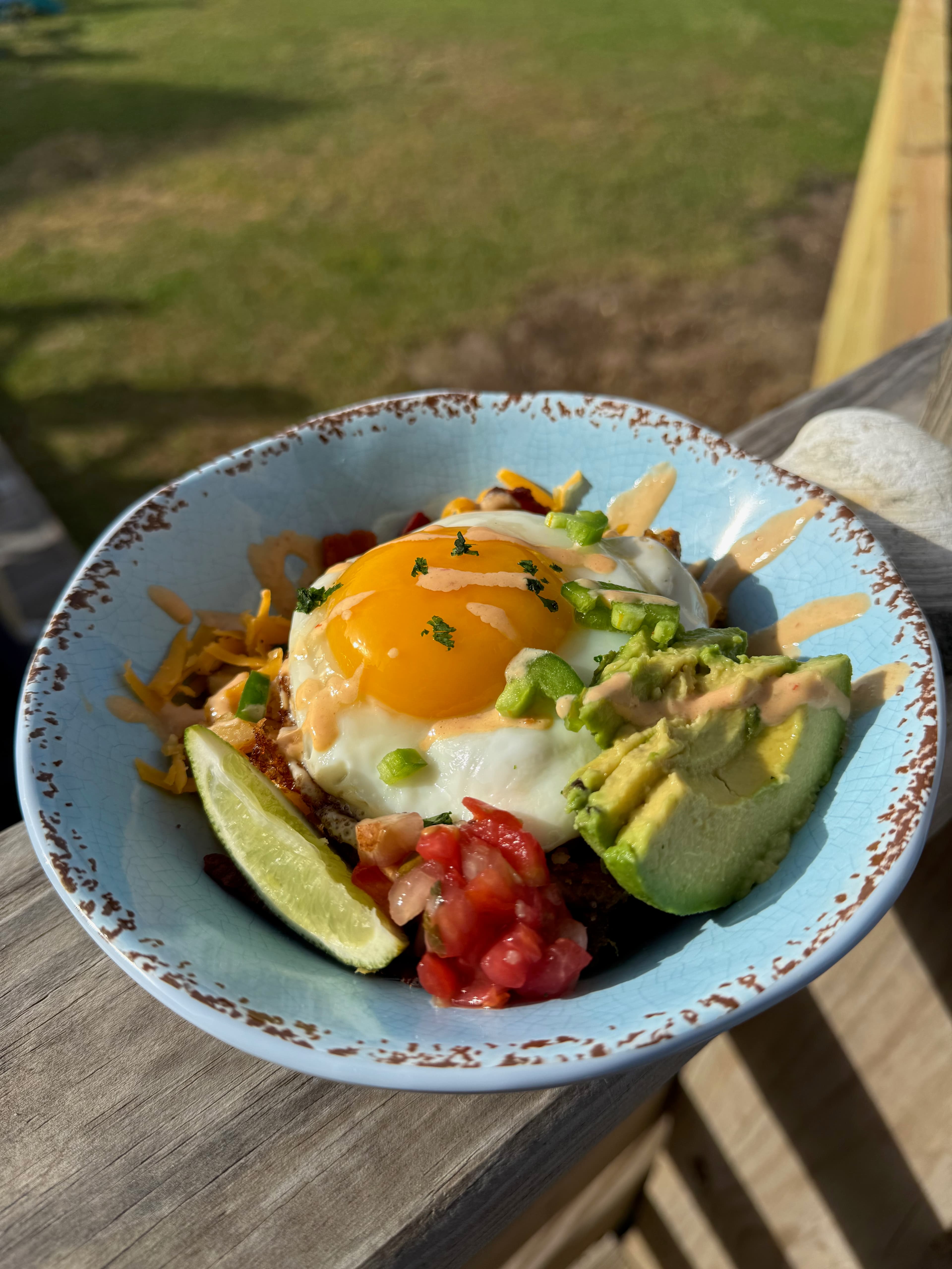 A bowl of eggs with a sunny-side-up yolk, avocado slices, diced tomatoes, cheese, and lime.