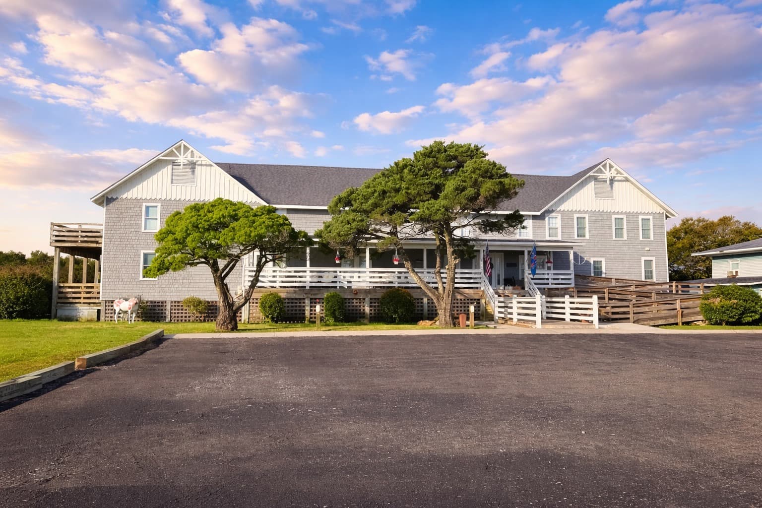 A large two-story gray house with a porch surrounded by greenery under a blue sky.