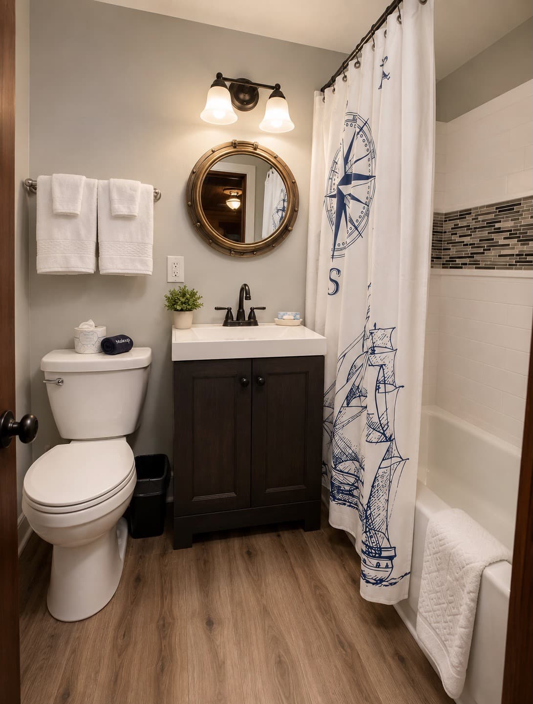 A compact bathroom featuring a nautical shower curtain, modern sink, and wooden flooring.