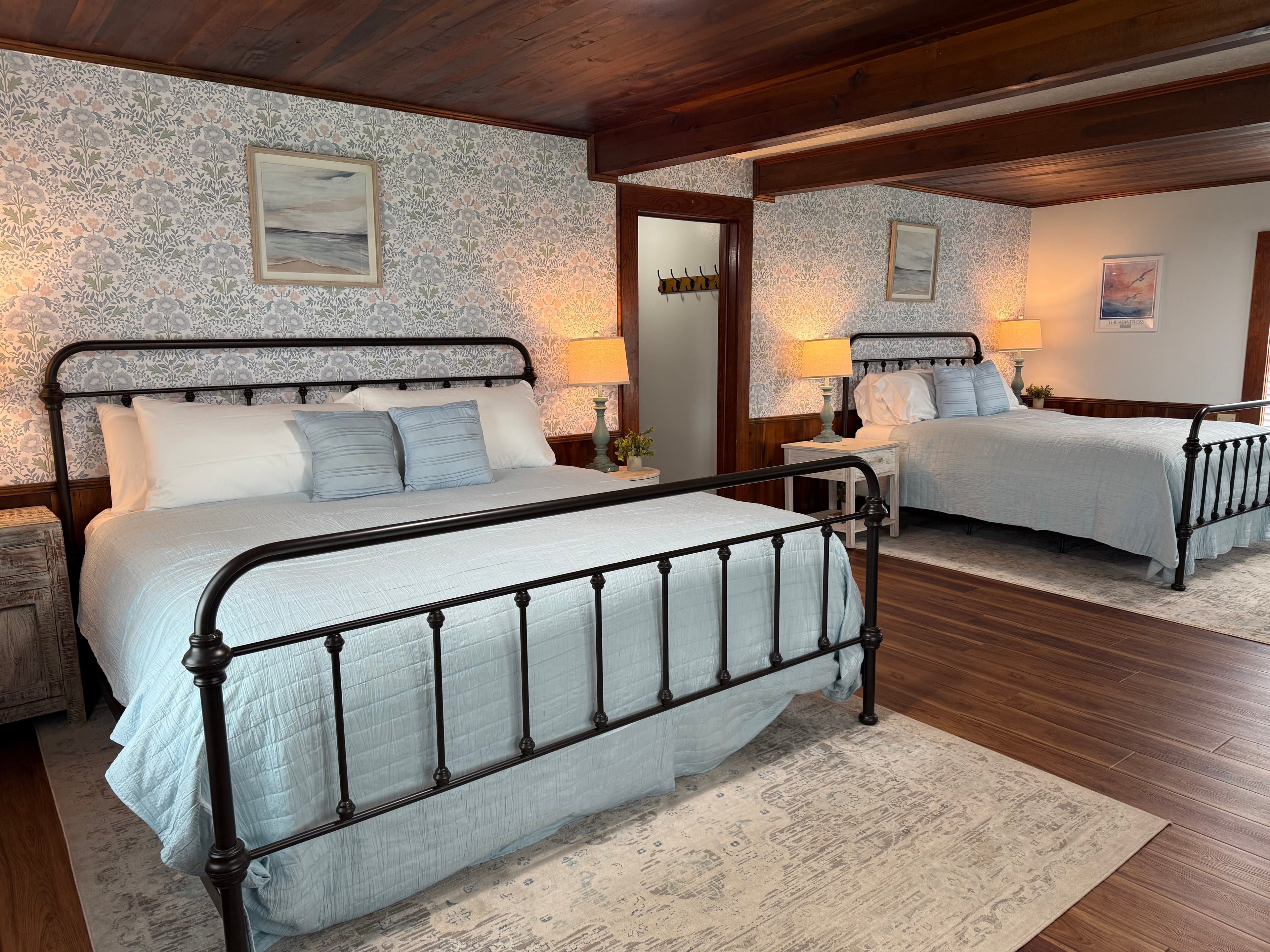 A cozy bedroom featuring two iron bed frames with light blue bedding and decorative wallpaper.