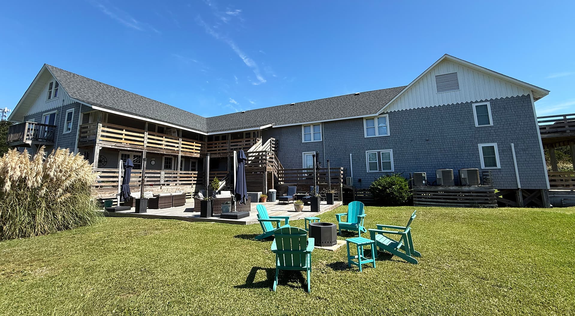 A modern building with a grassy area featuring colorful chairs and a fire pit.