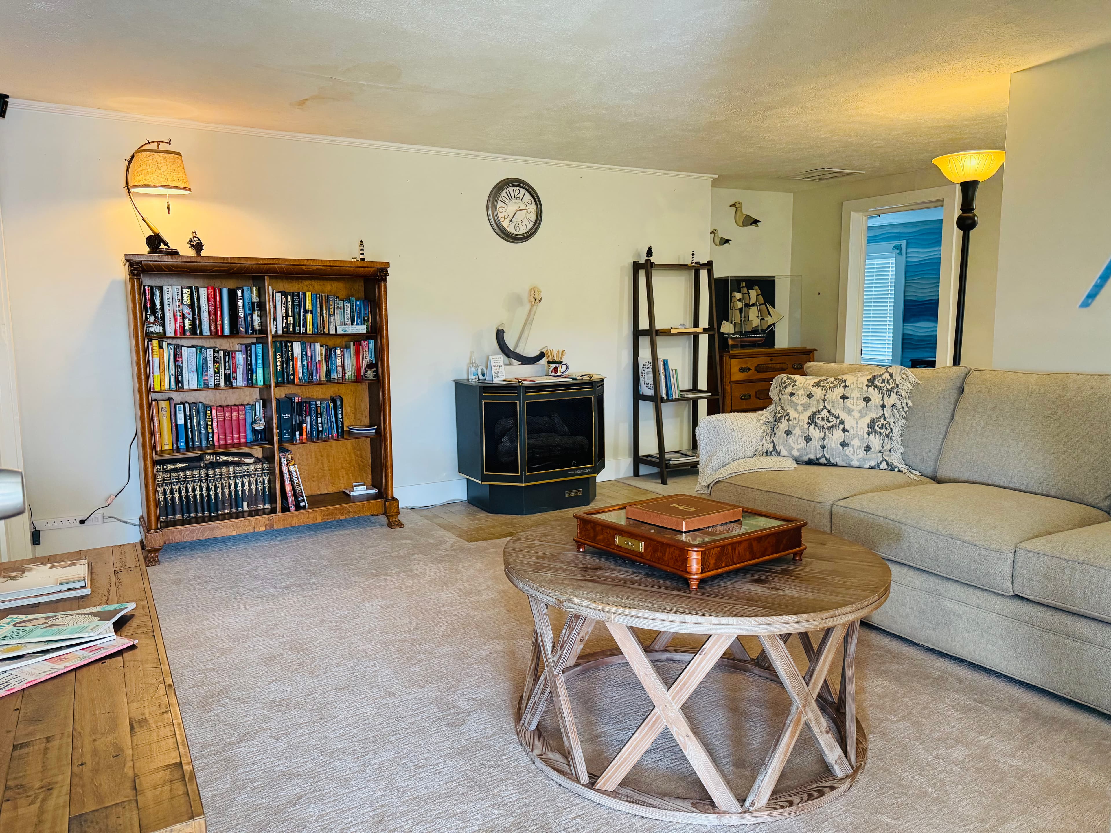 A cozy living room featuring a beige sofa, round wooden coffee table, bookshelf filled with books, and a fireplace.