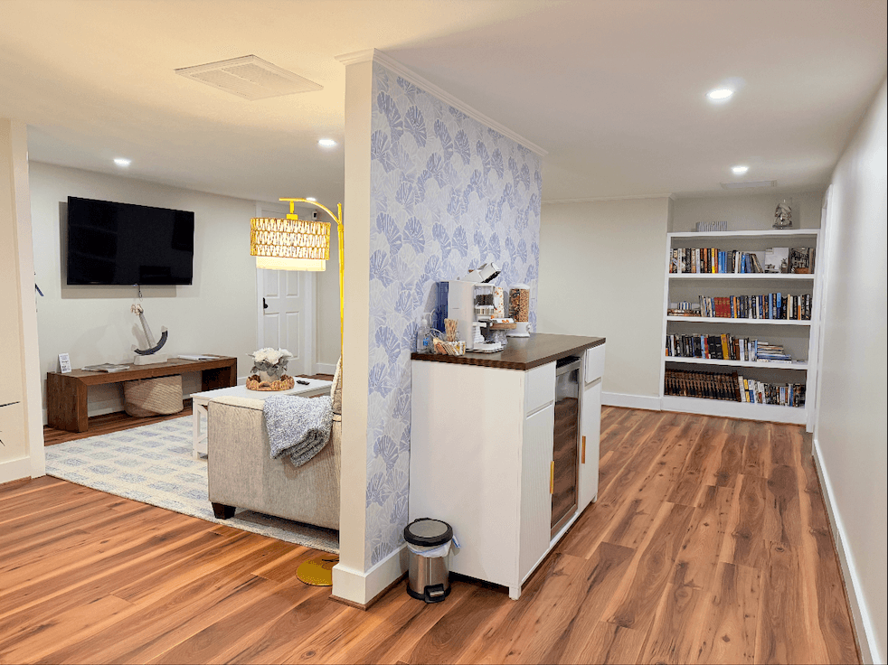 A modern basement interior featuring a kitchenette, a cozy seating area, and a bookshelf filled with books.