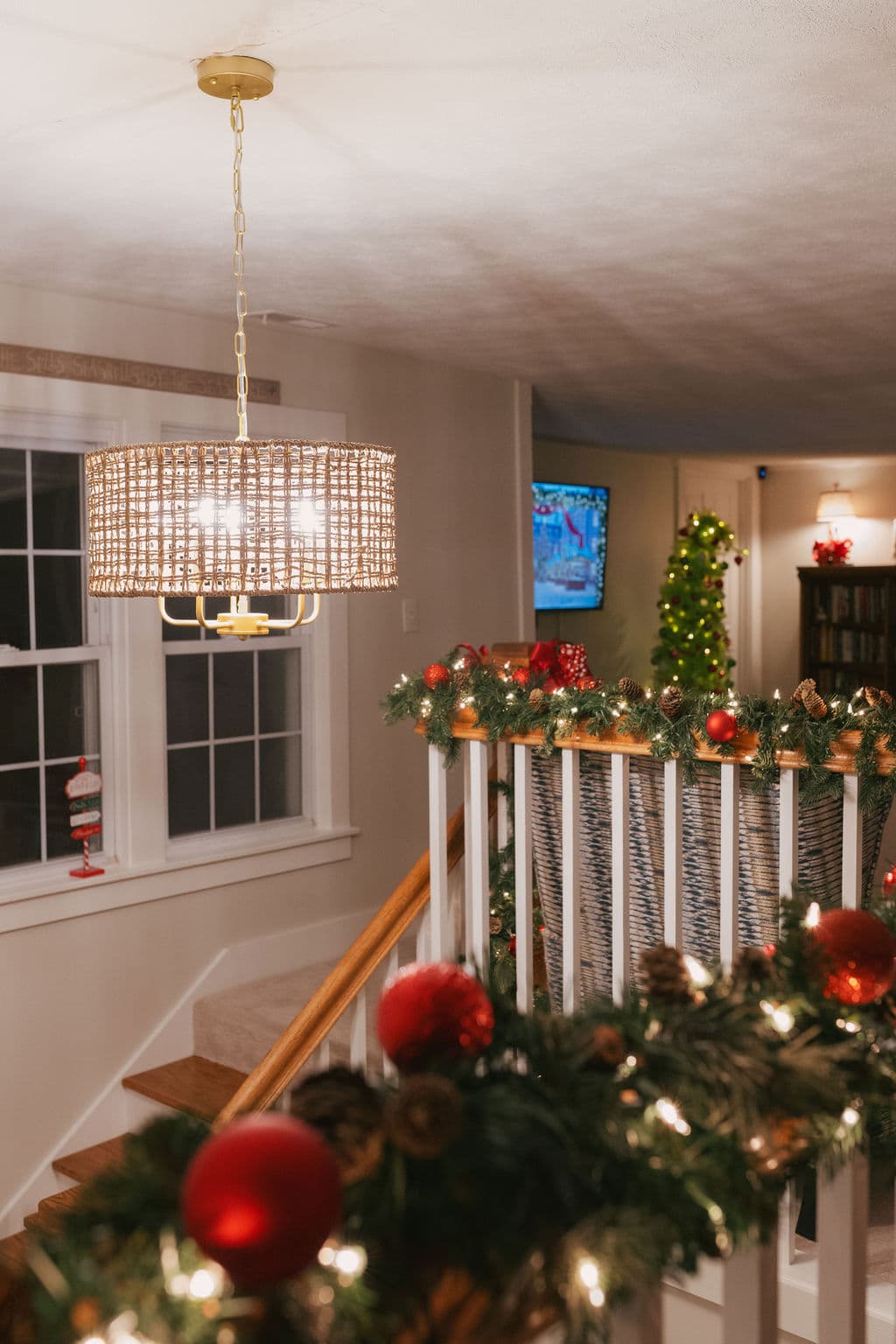 A warmly decorated staircase adorned with garland, ornaments, and a stylish pendant light.