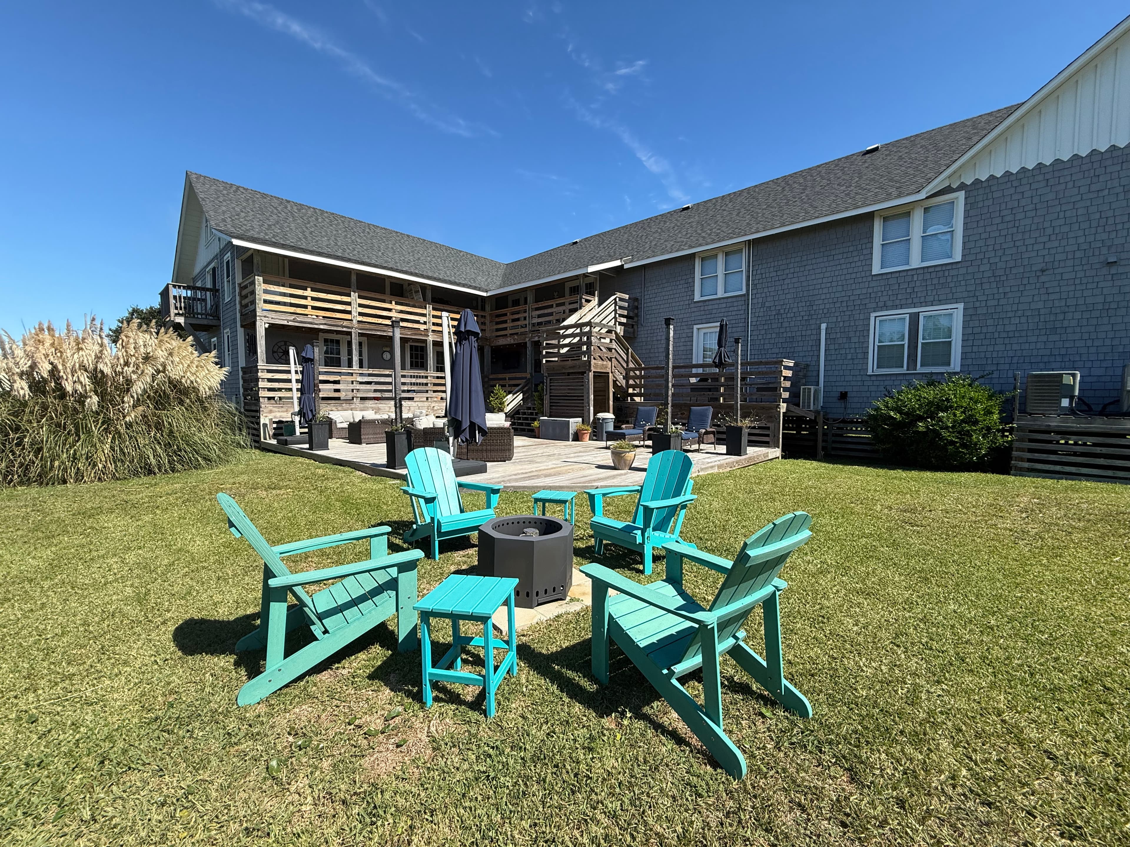 A patio area with teal Adirondack chairs and a fire pit, surrounded by grass and an apartment building.