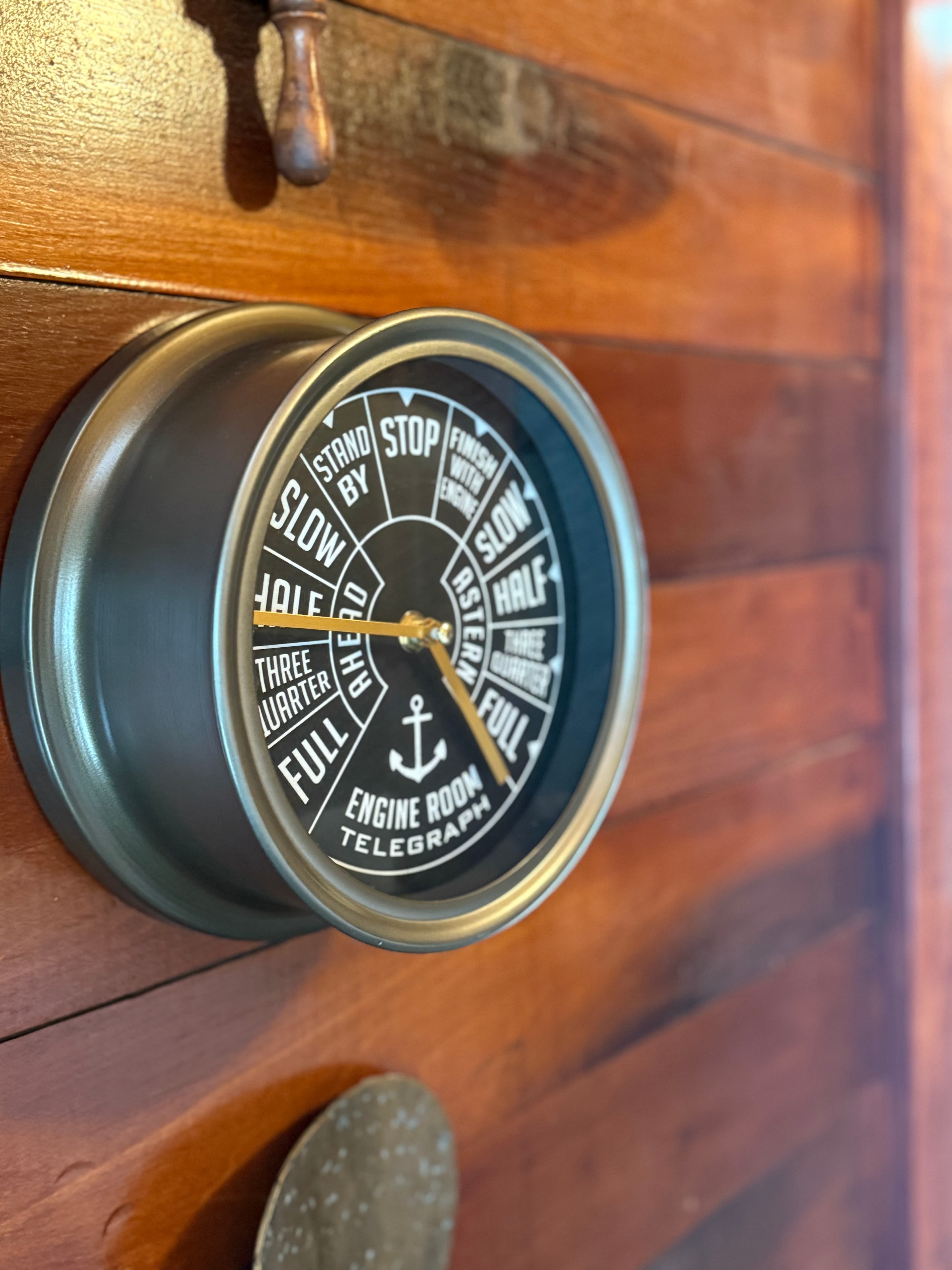 A vintage engine room telegraph with a dial displaying speed indicators mounted on a wooden wall.