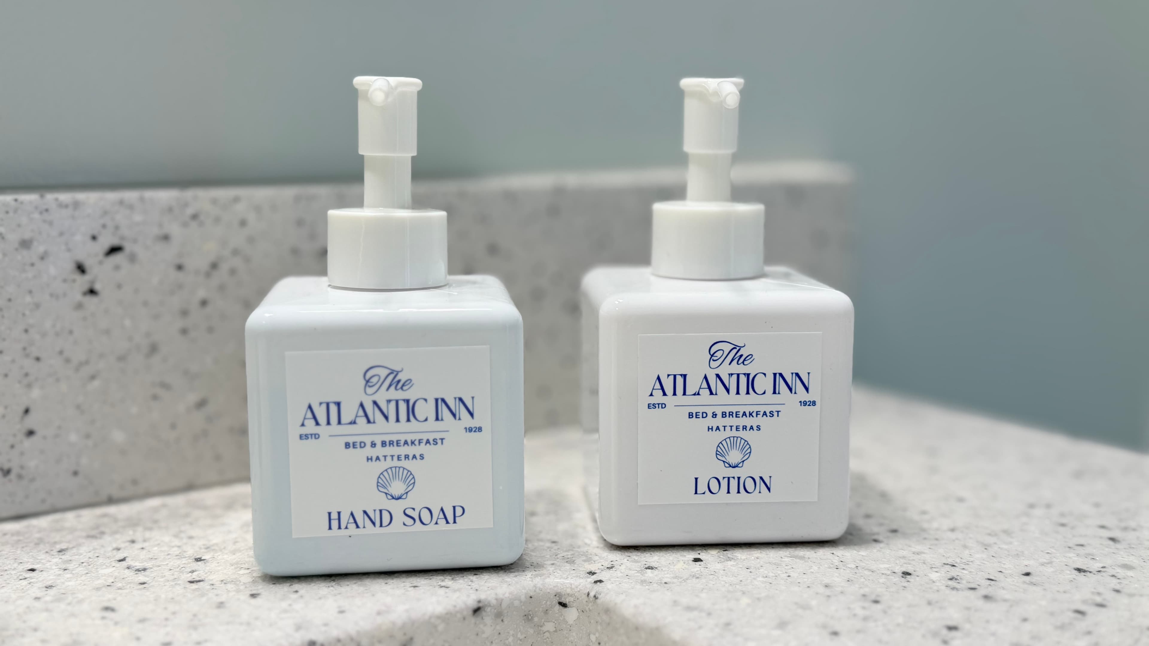 Two white pump bottles labeled "Hand Soap" and "Lotion" from The Atlantic Inn on a countertop.